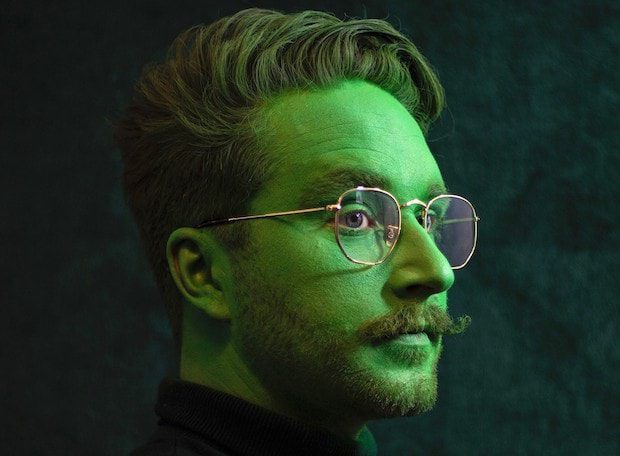 photo of a male presenting extraordinary learner wearing glasses, with a moustache and beard and a green glow on his face