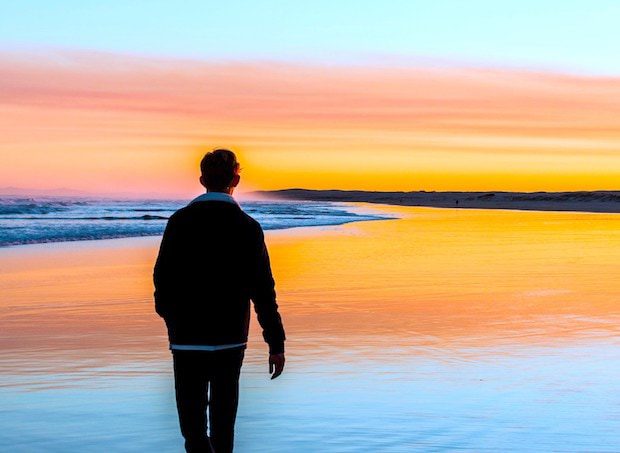 man walking down a beach toward the sunset contemplating lessons learned in life