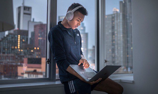 Man wearing headphones, leaning against a window sill with his laptop in hand, reading about Bitclout and Web 3.0 Social Media