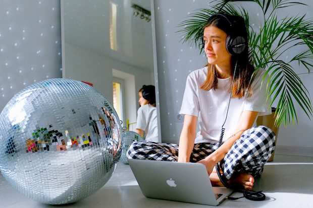 Woman sitting on floor behind lap top, next to large silver ball, and in front of mirror working on mastering flow states